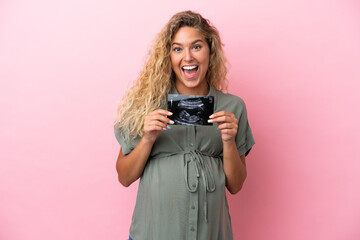 Girl with curly hair isolated on pink background pregnant and surprised while holding an ultrasound