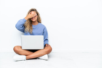 Girl with curly hair with a laptop sitting on the floor covering eyes by hands. Do not want to see something