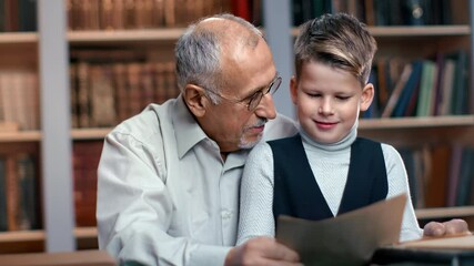 Happy old man grandfather and kid grandson learning antique historical paper documents at library
