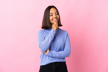 Young latin woman isolated on pink background looking to the side and smiling