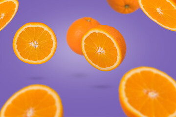 Minimal idea with whole and sliced orange flying in air  on purple background. Minimal fruit concept