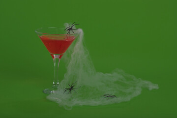 Red bloody cocktail  and bottle with cobweb or spider's  web on a green background.