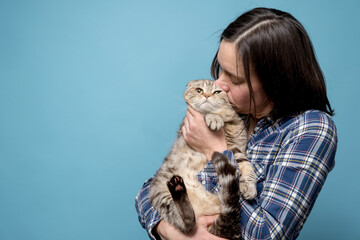 Woman hugs and kisses her adorable cat Scottish Fold. Concept of love and respect for animals. Copy space. Blue background.