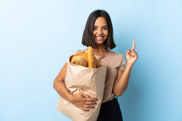 Young latin woman buying some breads isolated on blue background pointing up a great idea