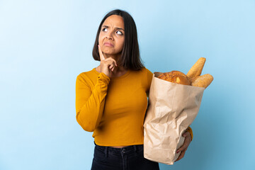 Young latin woman buying some breads isolated on blue background having doubts and thinking