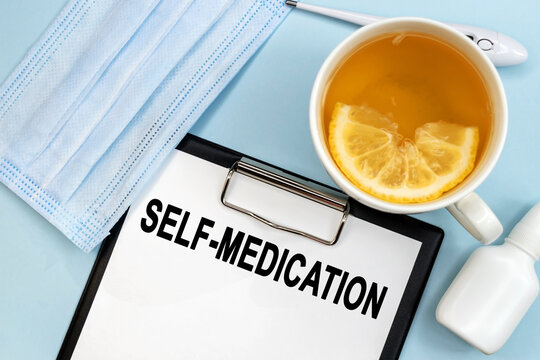 The word self-medication is written on a stationery tablet. Lemon tea and a medical mask with nose drops. Medical concept