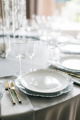 glass glasses and white plates. table setting in the interior of the restaurant. The decor of the festive table. In gray-silver tones with gold cutlery. Luxury wedding, party, birthday.