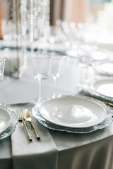 glass glasses and white plates. table setting in the interior of the restaurant. The decor of the festive table. In gray-silver tones with gold cutlery. Luxury wedding, party, birthday.