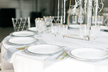 glass glasses and white plates. table setting in the interior of the restaurant. The decor of the festive table. In gray-silver tones with gold cutlery. Luxury wedding, party, birthday.
