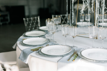 glass glasses and white plates. table setting in the interior of the restaurant. The decor of the festive table. In gray-silver tones with gold cutlery. Luxury wedding, party, birthday.