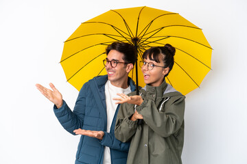 Young mixed race couple holding an umbrella isolated on white background extending hands to the...