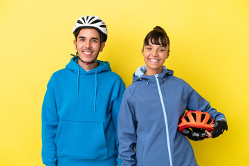 Young cyclist couple isolated on yellow background posing with arms at hip and smiling