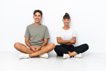 Fototapeta na wymiar Young mixed race couple sitting on the floor isolated on white background keeping the arms crossed in frontal position