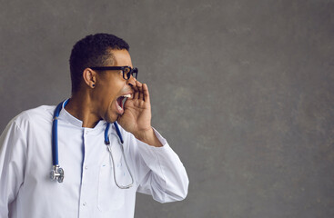 Young aggressive crazy african american doctor furious medical specialist with hand on mouth wearing uniform shouting screaming loudly looking aside to copy space announcing something