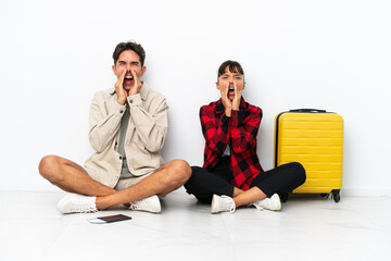 Obraz premium Young mixed race travelers couple sitting on the floor isolated on white background shouting and announcing something