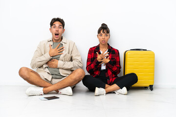 Obraz premium Young mixed race travelers couple sitting on the floor isolated on white background surprised and shocked while looking right