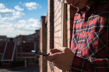 Caucasian man wearing a red plaid shirt chatting on his phone with a cloudy sky and houses at...