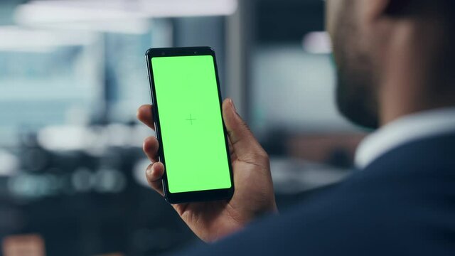 Black Businessman with Green Screen Chroma Key Smartphone in Office. African-American Businessperson using Internet, Social Media, Online Shopping with Mobile Phone Device. Over Shoulder