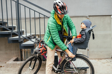 Young man adjusting son's protect for foot cycling in a bicycle seat with his father waiting for the riding at a street in city. Child safety and protection concept.