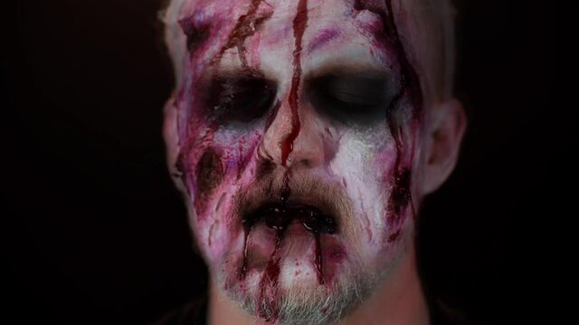 Creepy abstract nightmare glitch effect. Sinister man with horrible scary Halloween zombie makeup making faces, trying to scare, blood flows and drips on face. Dead guy with wounded bloody scars face