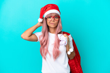 Young mixed race woman handing out gifts on Christmas isolated on blue background having doubts