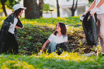 Team of three people participate in gathering the garbage outdoors in voluntary mission, making fun and smiling. © Viorel