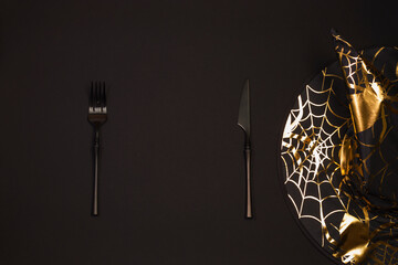 Halloween holiday. Serving on a dark table with a black pointed conical witch hat and black cutlery. Flat lay, top view trendy holiday concept. Copy space.