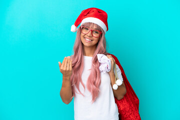 Young mixed race woman handing out gifts on Christmas isolated on blue background inviting to come with hand. Happy that you came