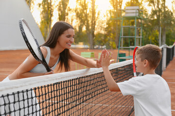Little boy giving high five to his mother on tennis court