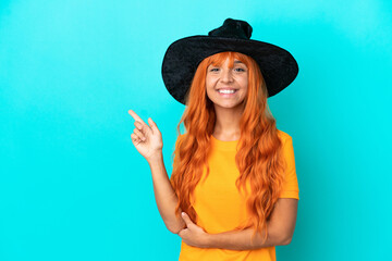 Young woman disguised as witch isolated on blue background pointing finger to the side