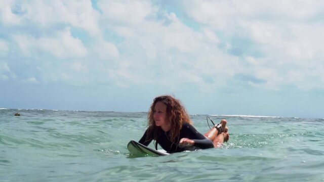 Video footage of surfer girl on white surf board in blue ocean pictured from the water in Bali