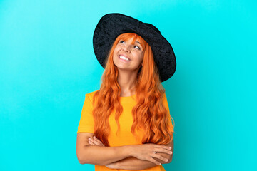 Young woman disguised as witch isolated on blue background looking up while smiling