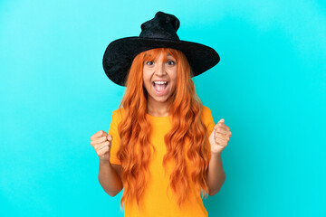 Young woman disguised as witch isolated on blue background celebrating a victory in winner position