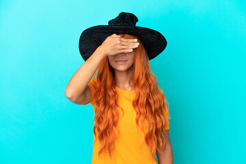 Young woman disguised as witch isolated on blue background covering eyes by hands. Do not want to see something