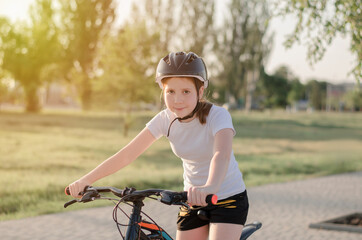 An 11-year-old girl in a protective sports helmet sits on a bicycle. Girl with a bike in the park. Children's sports and a healthy lifestyle