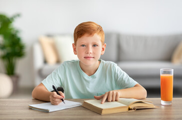 Adorable redhead boy reading book and writing notes
