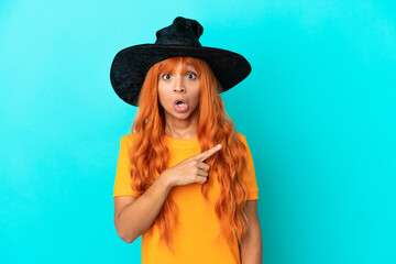 Young woman disguised as witch isolated on blue background surprised and pointing side