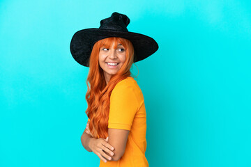 Young woman disguised as witch isolated on blue background with arms crossed and happy