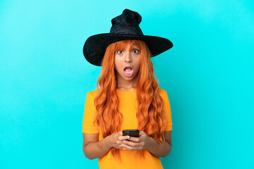 Young woman disguised as witch isolated on blue background surprised and sending a message