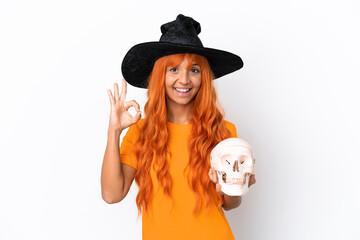 Young mixed race woman disguised as witch holding a skull isolated on white background showing ok sign with fingers