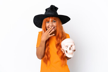 Young mixed race woman disguised as witch holding a skull isolated on white background happy and smiling covering mouth with hand