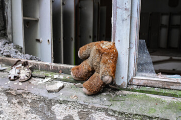 a headless teddy bear sits on a window sill in a ruined building