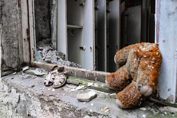 a headless teddy bear sits on a window sill in a ruined building