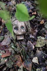 dirty torn off doll head lying on the ground in the woods