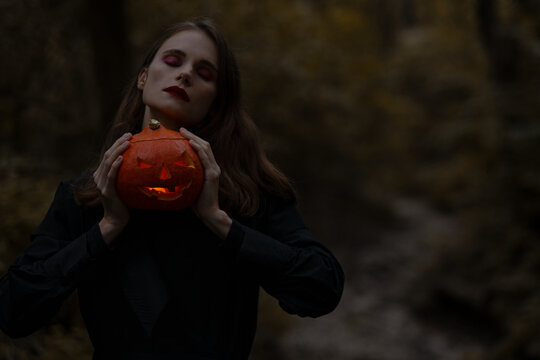 Portrait of young skinny woman, holding glowing Jack O Lantern pumpkin in the wood
