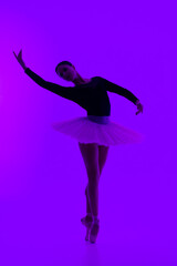 Beautiful ballerina on purple background dancing ballet. Woman performs smooth movements. Sensual dancer in tutu dress on scene under neon light.. 