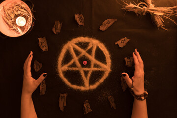 brujería, oráculo o lectura con runas de madera, estrella pentagonal de arena con manos de mujer sobre fondo negro, velas y amuletos © Galdys V