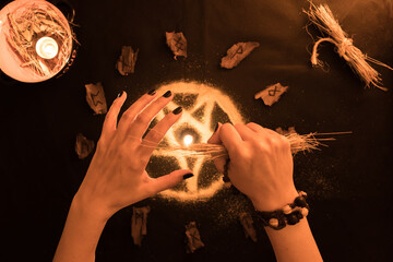 brujería, oráculo o lectura con runas de madera, estrella pentagonal de arena con manos de mujer sobre fondo negro, velas y amuletos © Galdys V
