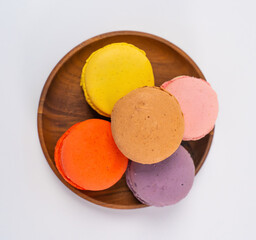 Multicolored macarons on a wooden plate on a white background.