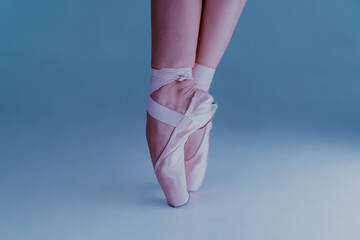 Ballet dancer's feet, how she practices in pointe shoes exercises on blue background. Beautiful woman's legs. Ballerina shows classic ballet pas.